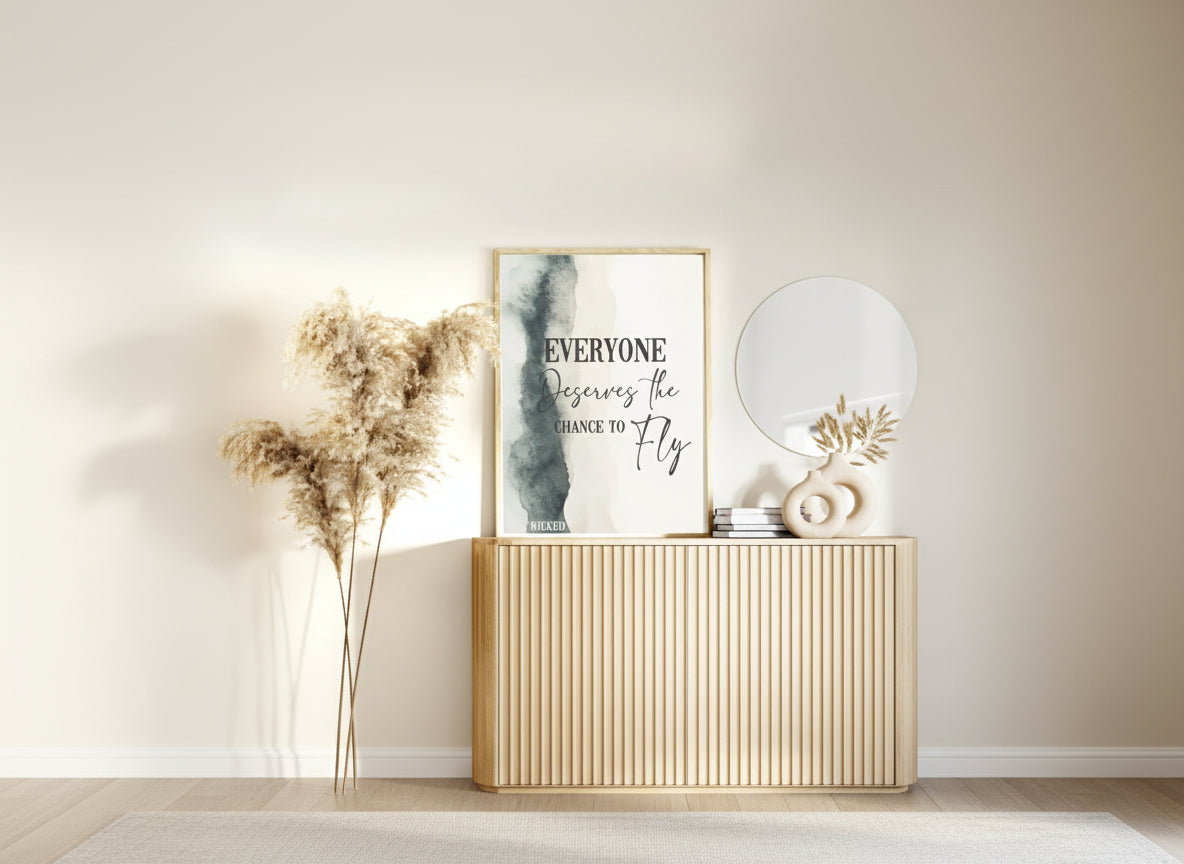 Decorative interior setting with a cabinet, mirror, and framed Wicked Movie quote on a beige wall.